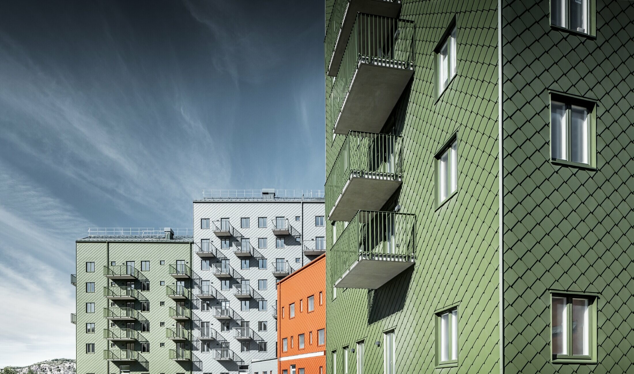 Różne bloki mieszkalne obok siebie z poszyciem z rombu fasadowego PREFA 29 × 29 w kolorze ceglastym, oliwkowym i jasnoszarym.