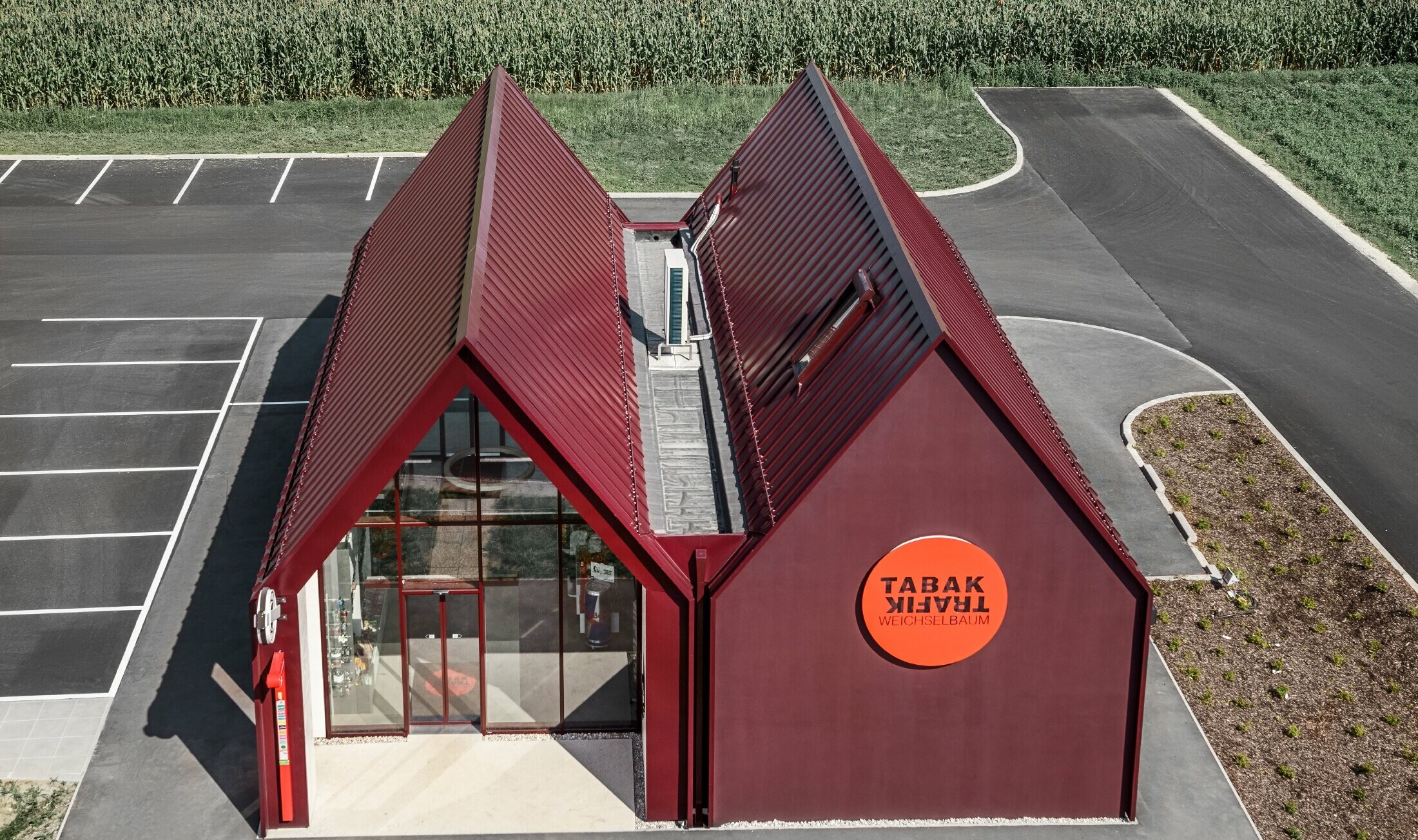 Nowoczesny sklep tytoniowy z dachem dwuspadowym bez okapu, z okładziną aluminiową PREFA wykonaną w systemie pionowych i kątowych zakładek w kolorze specjalnym czerwono-czarnym