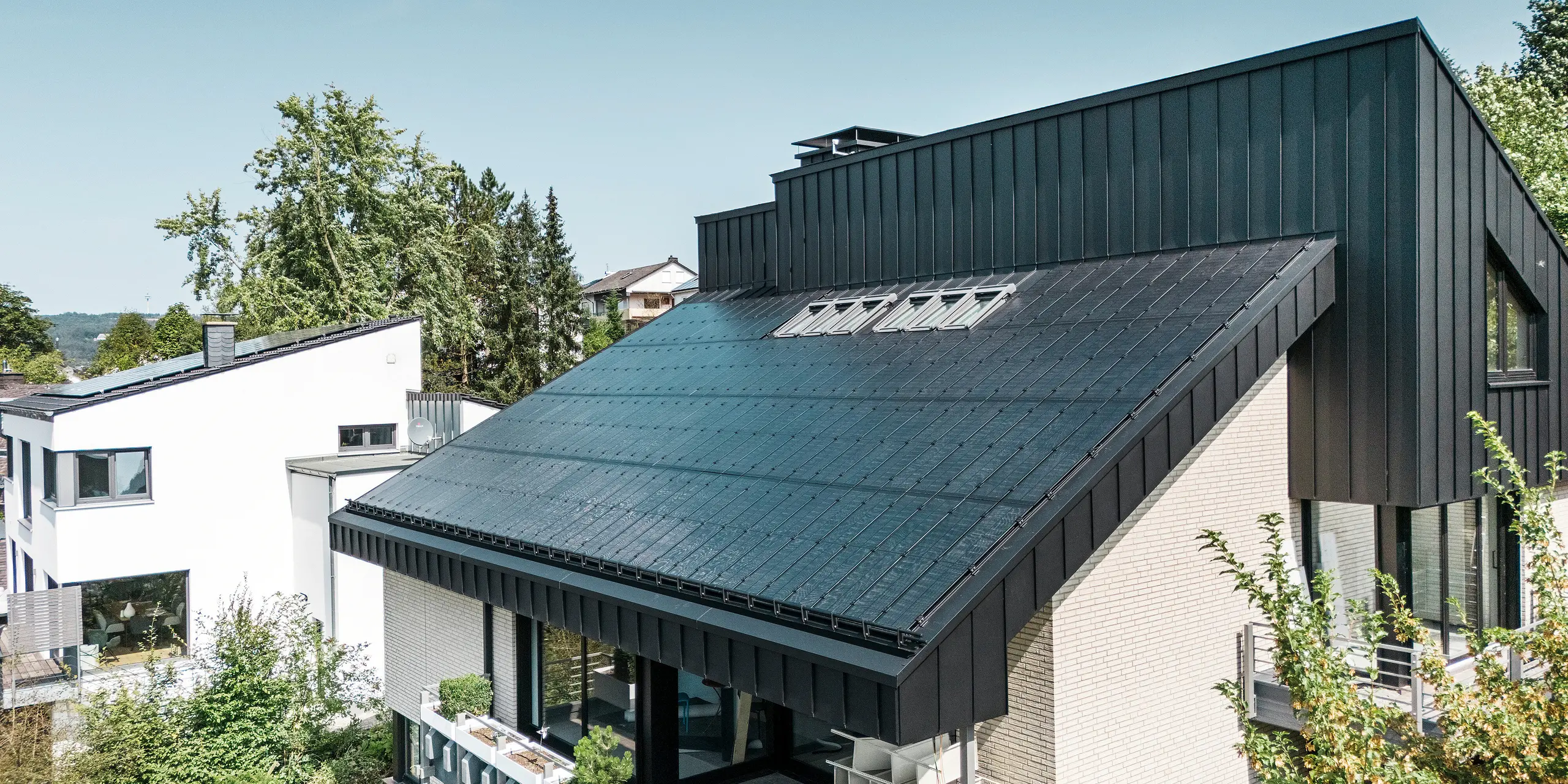 Nowoczesna architektura domu jednorodzinnego w Meschede w Niemczech, z dachem aluminiowym PREFALZ w kolorze P.10 czarny i zintegrowanymi modułami fotowoltaicznymi szkło/szkło. Dach z przesunięciem łączy w sobie ponadczasowy design z zrównoważoną technologią fotowoltaiczną. Innowacyjne moduły solarne PREFALZ zapewniają moc 18 kWp. Bezramowe moduły oraz eleganckie aluminium pokrycie dachowe i elewacyjne tworzą estetyczną i funkcjonalną całość, która harmonijnie wtapia się w zielone otoczenie.