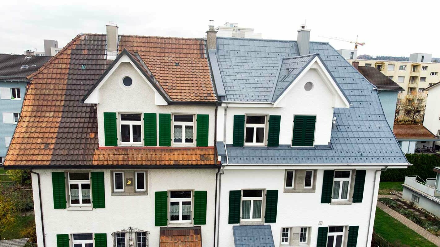 Połowa bliźniaka w Szwajcarii; lewa część budynku nie została jeszcze zmodernizowana i jest pokryta dachówką plamistą. Prawa część budynku została pokryta płytami dachowymi PREFA w kolorze szarym kamiennym.